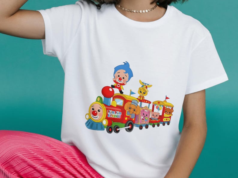 Puede incluir: Camiseta blanca con un gr&aacute;fico colorido de un tren de dibujos animados con personajes. El tren es rojo, amarillo y azul, con el texto "Plim Plim & Friends". La camiseta tiene mangas cortas.