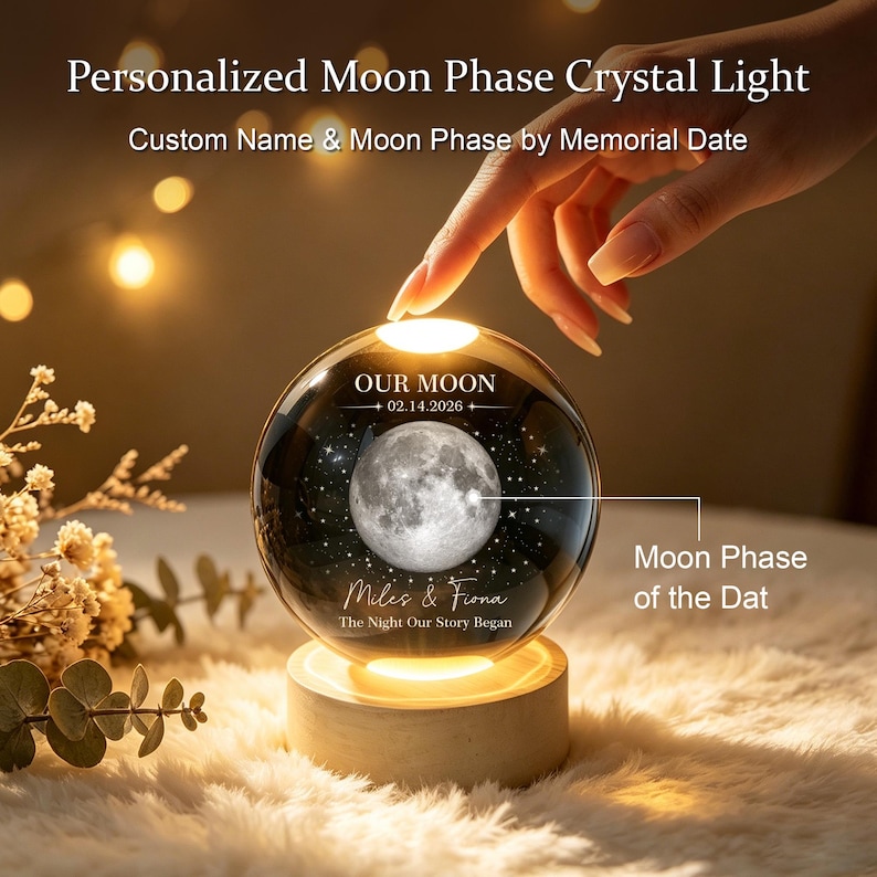 Op de afbeelding: Een bolvormige kristallen lamp met een gegraveerde maanfase, de tekst OUR MOON, 02.14.2026, Miles & Fiona en The Night Our Story Began. De heldere glazen bol staat op een ronde houten voet die het ontwerp aan de binnenkant van onderaf verlicht.