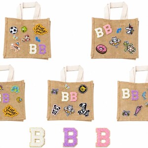 May include: Five beige tote bags with white handles, each decorated with patches and the letters "BB". Patches include a soccer ball, butterflies, and a car. The phrase "Keep Smiling You" is also visible.