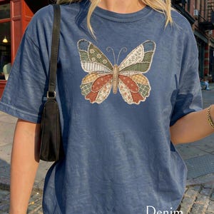 以下が含まれることがあります： パッチワークの蝶のデザインが特徴のデニムブルーのTシャツ。蝶は、花柄やチェック柄など、さまざまな色と模様の羽を持っています。「Denim」の文字がシャツの下部にプリントされています。