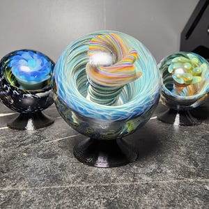 May include: A set of three ceramic nesting bowls in shades of blue, green, and white. The bowls feature a speckled glaze and a simple, modern design. The largest bowl is approximately 6 inches in diameter.