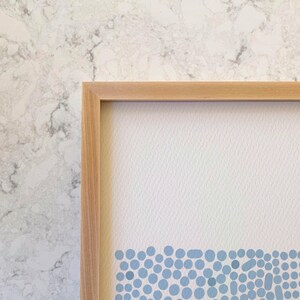 May include: A framed print with a light blue and white abstract design. The design features a row of small, blue circles at the bottom of the print.