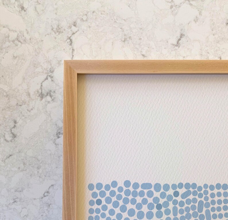 May include: A framed print with a light blue and white abstract design. The design features a row of small, blue circles at the bottom of the print.