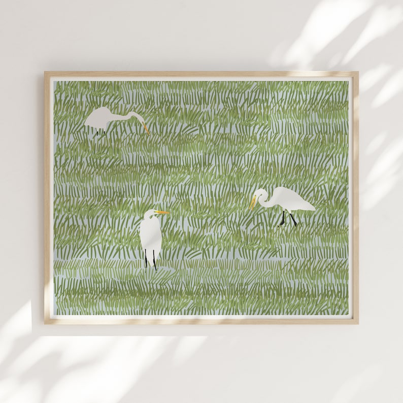 May include: A framed print of three white egrets standing in a field of green grass. The egrets are depicted in a stylized, graphic style.