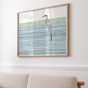 May include: A framed print of a gray heron standing on a blue and green striped background. The heron has an orange beak and is facing to the right.