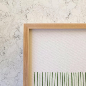 May include: A framed print with a white background and a green abstract design at the bottom. The frame is made of light wood.