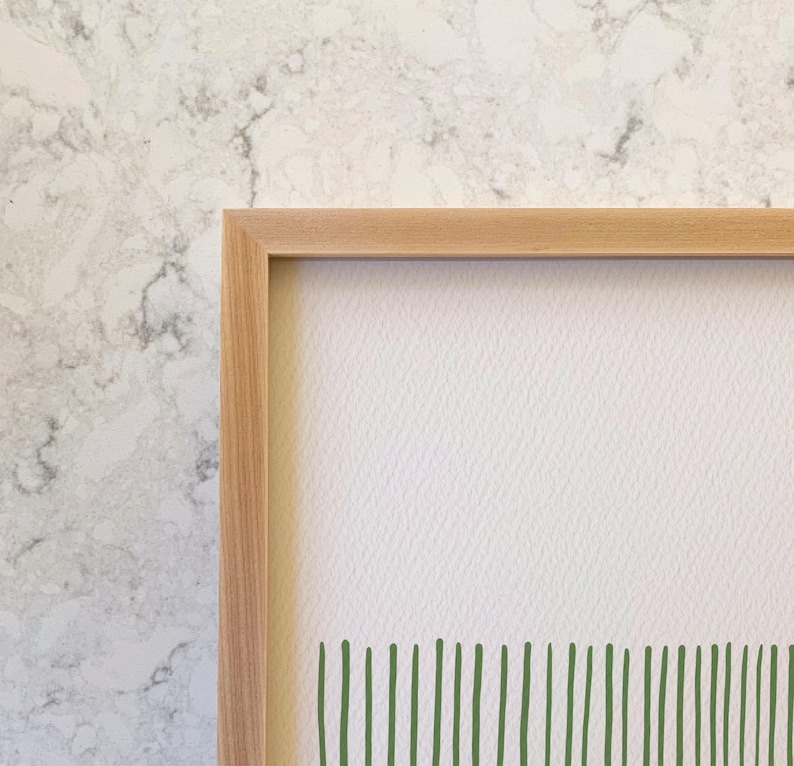 May include: A framed print with a white background and a green abstract design at the bottom. The frame is made of light wood.