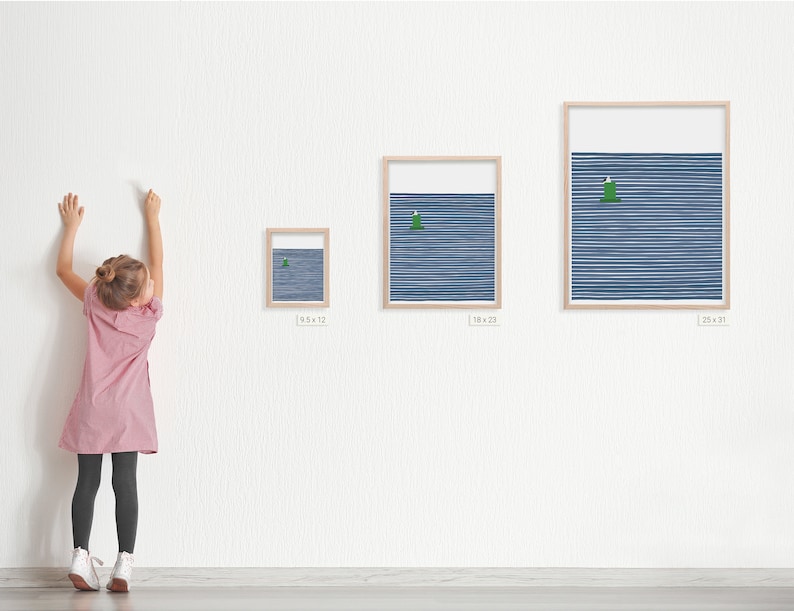 a young girl standing next to three framed art prints by artist jorey hurley. the prints are different sizes . the image on the prints is a coastal scene of a seagull sitting on a buoy with a navy blue striped background.