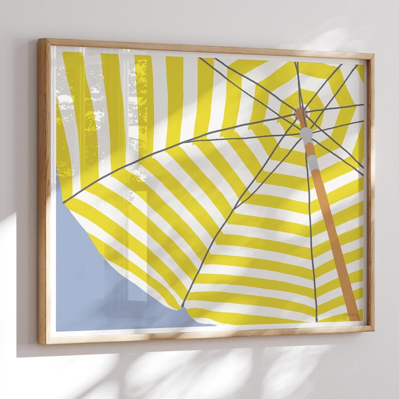 May include: A framed art print depicting a yellow and white striped beach parasol. The parasol is partially open, set against a light blue backdrop. The wooden frame provides a natural aesthetic to the artwork.