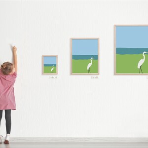 May include: Three framed prints of a white egret standing on a green grassy area with a blue ocean in the background. The prints are in different sizes, with the smallest measuring 9.5 inches by 12 inches, the middle measuring 18 inches by 23 inches, and the largest measuring 25 inches by 31 inches.