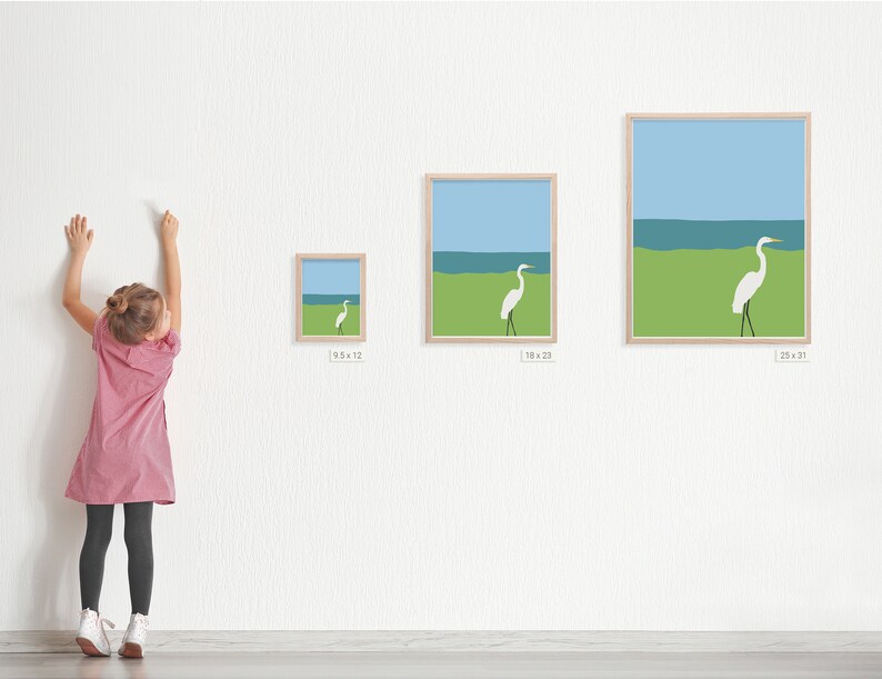May include: Three framed prints of a white egret standing on a green grassy area with a blue ocean in the background. The prints are in different sizes, with the smallest measuring 9.5 inches by 12 inches, the middle measuring 18 inches by 23 inches, and the largest measuring 25 inches by 31 inches.