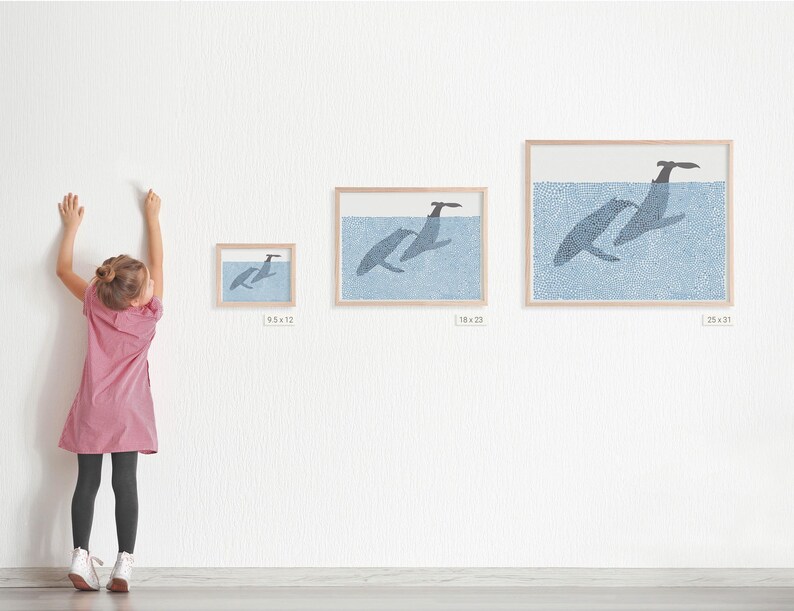 May include: Three framed prints of whales jumping out of the water. The prints are in different sizes, with the largest print measuring 25 x 31 inches. The prints are on a white wall, and a young person is standing in front of them.