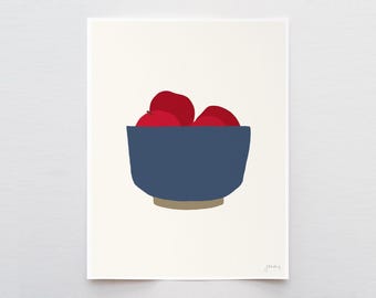 May include: A minimalist art print on a cream background featuring a deep blue bowl filled with three bright red apples. The bowl has a tan base and a simple, clean design. The artist's signature is visible in the bottom right corner of the print.
