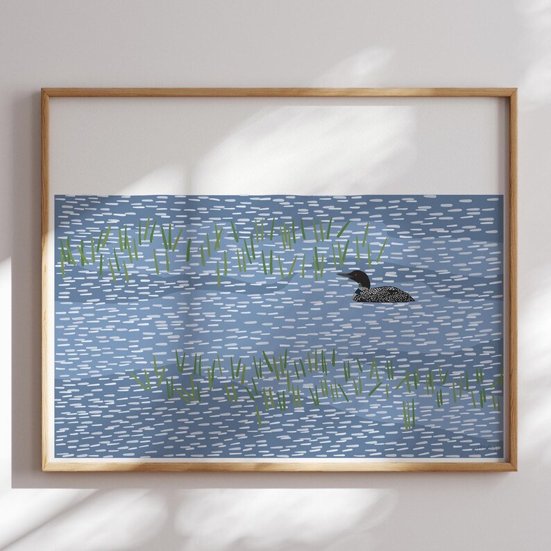May include: A framed wall art print featuring a stylized illustration of a black and white loon swimming in blue water with small white dashes representing ripples and scattered green vertical lines depicting aquatic vegetation.
