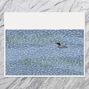 May include: A rectangular art print featuring a stylized illustration of a black and white loon swimming in blue water with white dash patterns and green reeds. The artwork is centered on a white background with a clean, flat graphic design.