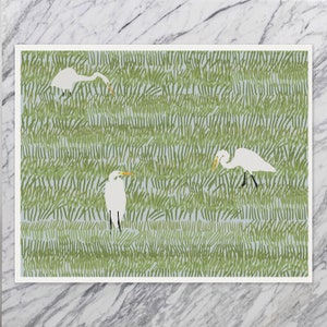 May include: A digital illustration of three white egrets standing in a field of green grass. The egrets have long, slender necks and legs, and their beaks are yellow. The grass is drawn with short, thin lines, creating a textured effect.