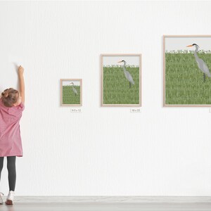 May include: A framed print of a grey heron standing in a field of green grass. The print is available in three sizes: 8x12 inches, 18x23 inches, and 25x31 inches.