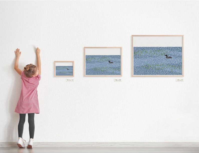 May include: Three framed wall art prints featuring a loon swimming on a blue patterned lake with green reeds. The frames are labeled with dimensions 9.5x12, 18x23, and 25x31 inches, displayed in a horizontal row on a white wall.