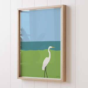 May include: A framed illustration of a white egret standing on a green grassy area with a blue ocean in the background.