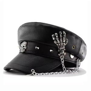 May include: Black leather hat with a flat top and a short brim. The hat is decorated with silver-coloured skull and skeleton hand charms, along with silver spikes. A silver chain hangs from the side of the hat.