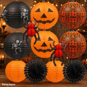 May include: A collection of Halloween decorations including round paper lanterns in black with white skeleton prints, orange with jack-o'-lantern faces, and orange with black damask patterns, plus red honeycomb spiders and black paper fans.