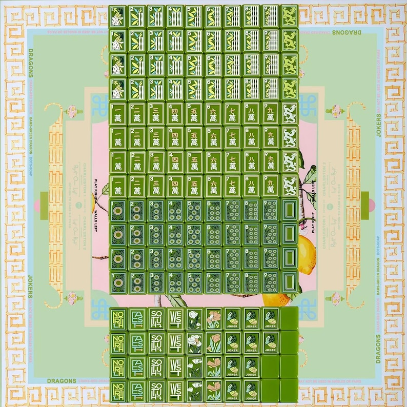 May include: A Mahjong set featuring green tiles with white and green engraved symbols, numbers, and characters. The tiles are arranged in a grid on a light green mat with a decorative border and illustrations of lemons and foliage.