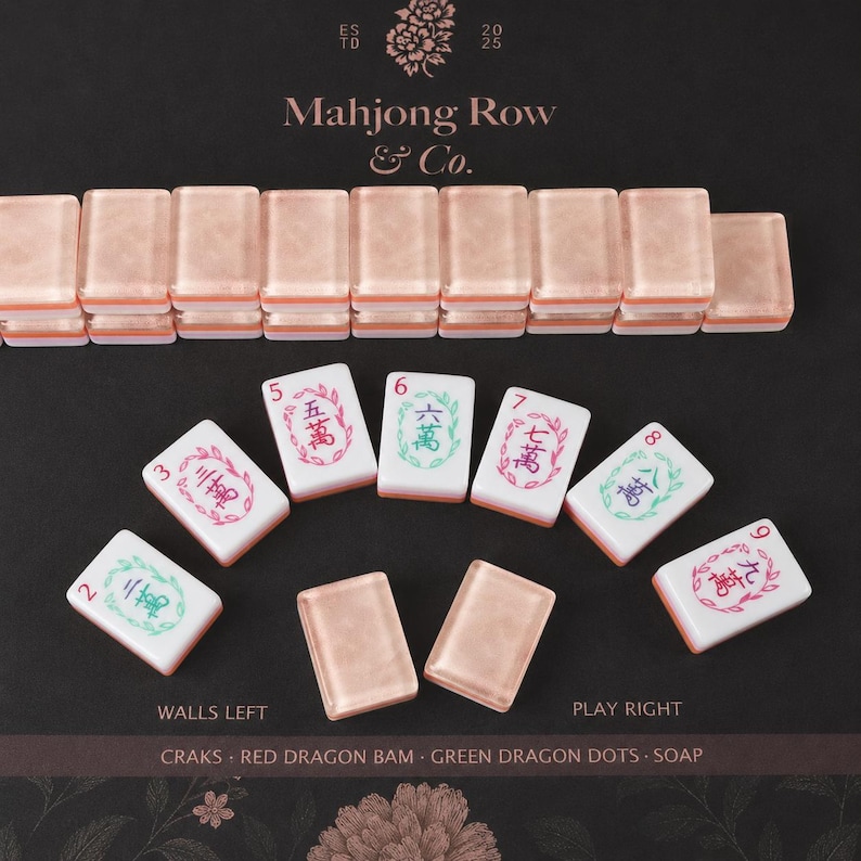 Puede incluir: Un juego de fichas de Mahjong con una fila de fichas de oro rosa en la parte superior y fichas blancas individuales con caracteres chinos coloridos y bordes florales debajo. El texto Mahjong Row & Co. est&aacute; impreso arriba con etiquetas.