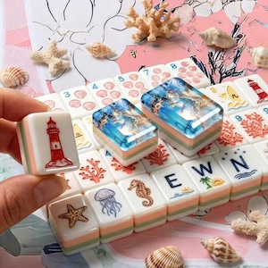 May include: A set of rectangular mahjong tiles featuring nautical and ocean-themed illustrations including a red and white lighthouse, a starfish, a jellyfish, a seahorse, and the letters E, W, and N. Two tiles display a blue resin ocean scene.