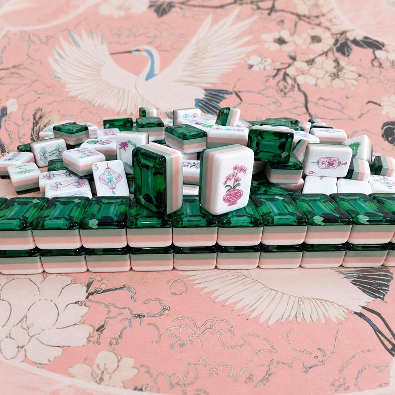 May include: A collection of mahjong tiles featuring a layered design with a translucent emerald green top, a pale green middle, and a white base. Some tiles display floral illustrations and Chinese characters in pink and black ink on the white face.