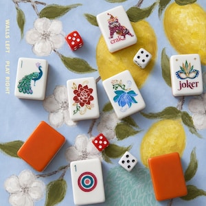 May include: A set of white mahjong tiles with colorful illustrations including a peacock, a red flower, a blue flower, a dragon, and a joker mask, alongside two solid orange tiles, three red and white dice, and tiles with a bullseye and the number 1.