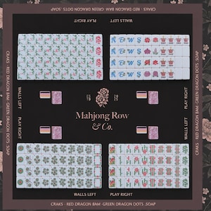 以下が含まれることがあります： Mahjong Row & Co.のゲームマット。カラフルなシンボル、数字、文字が描かれた白い牌が4つのセクションに分かれて配置されています。暗い背景には花柄、ゲームプレイ用のラベル、中央にブランド名が記されています。