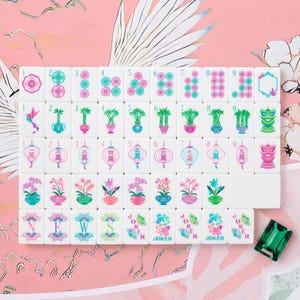 May include: A set of white mahjong tiles featuring colorful floral, bamboo, lantern, and character designs in pink, green, and blue. The tiles include numbered sequences, directional markers, and joker tiles, accompanied by a single green gem tile.