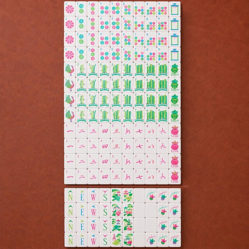May include: A complete set of white Mahjong tiles arranged in a grid. The tiles feature colorful engraved designs including bamboo stalks, Chinese characters, floral patterns, directional letters N, E, W, S, and tiles labeled Joker, Bam, and Crak.