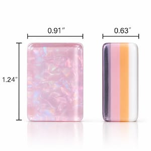 以下が含まれることがあります： 2つの長方形の樹脂製ピース。左側のピースはピンク色で虹色の質感があり、幅2.31cm、高さ3.15cmです。右側のピースはダークパープル、ピンク、オレンジ、白の縦縞模様で、幅は1.60cmです。