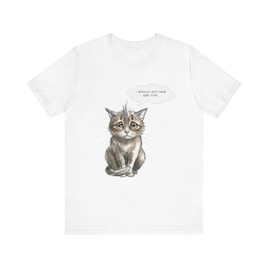 May include: White t-shirt featuring a cartoon illustration of a sad-looking cat. The cat is depicted in shades of gray and brown, with large, expressive eyes. A thought bubble above the cat reads, "I SHOULD NOT HAVE SAID THAT..."