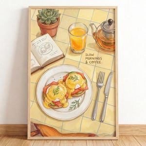 May include: A framed illustration on a yellow checkered tablecloth featuring two eggs benedict on a white plate, a glass of orange juice, a glass teapot, an open book, and a potted succulent. The text SLOW MORNINGS & COFFEE. is printed on the table.