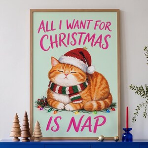 May include: A framed wall art print featuring a ginger tabby cat wearing a red and white Santa hat and a red, white, and green striped scarf. The cat is lying down with eyes closed. The text reads ALL I WANT FOR CHRISTMAS IS NAP in pink.