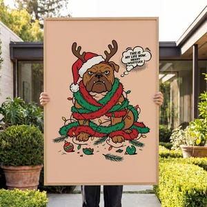 May include: A rectangular framed print on a light peach background featuring a brown bulldog wearing a red Santa hat with reindeer antlers and green tinsel. A speech bubble contains the text: This is my life now. Merry whatever.