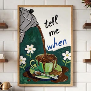 May include: A framed wall art print featuring a silver moka pot pouring dark coffee into a light green cup on a saucer. The text "tell me when" is written in black and blue. The background is dark green with white flowers and spilled coffee.