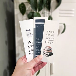 May include: Three rectangular bookmarks are held in a hand. One features an owl illustration and the text "OWL KEEP YOU PLA". Another has a book design and the text "GO AWA I'M REA ING". The third bookmark has a stack of books and the text "BOOKS ARE MY HAPPY PLACE".