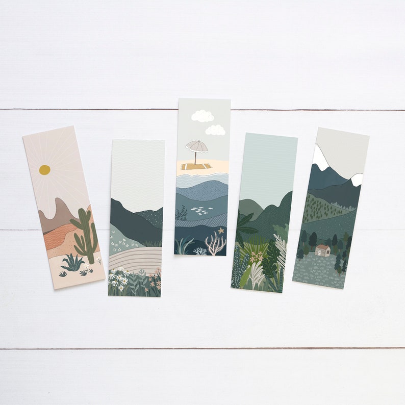 May include: Five rectangular bookmarks featuring landscape illustrations. Designs include a desert scene with a sun and cactus, a mountain range, a beach scene with an umbrella, and a forest with a small house. The bookmarks are on a white wooden surface.