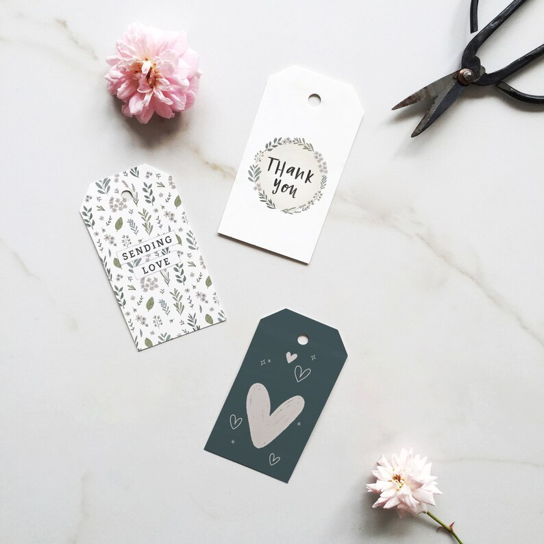 May include: Three gift tags with different designs. One tag says "Thank you" inside a wreath. Another says "Sending Love" with floral patterns. The third tag has a large heart and small hearts. A pair of scissors and flowers are also in the image.