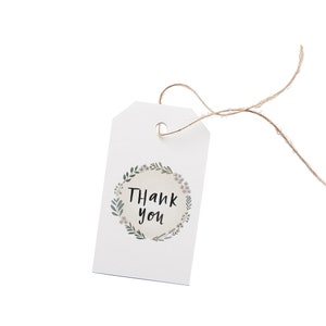 May include: A white gift tag with a floral wreath design and the words "Thank you" in black script. The tag is attached to a natural twine string, perfect for adding a personal touch to gifts or favors.