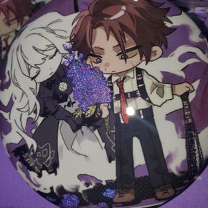 May include: A circular pinback button featuring a stylized anime illustration of a brown-haired character in a white shirt and black harness, standing next to a white-haired figure. The design includes purple glitter accents and a red tie.