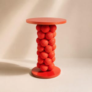 Könnte beinhalten: Ein leuchtend orangefarbener Beistelltisch mit einer glatten, kreisförmigen Tischplatte und einem passenden runden Fuß. Die zentrale Stützsäule besteht aus einer dichten Ansammlung texturierter, kugelförmiger Elemente in einheitlichem Orange.