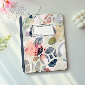 May include: Composition book with a colorful abstract design. The cover features a pattern of organic shapes in shades of pink, blue, gray, and yellow. The title "COMPOSITION BOOK" is printed on a white label. The book measures 7.5 in x 9.75 in.