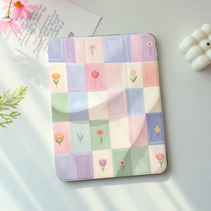 May include: A pastel-colored tablet case with a floral pattern. The case features a grid design with squares in shades of pink, purple, blue, and green, each adorned with a different flower illustration. The case is designed to protect a tablet.