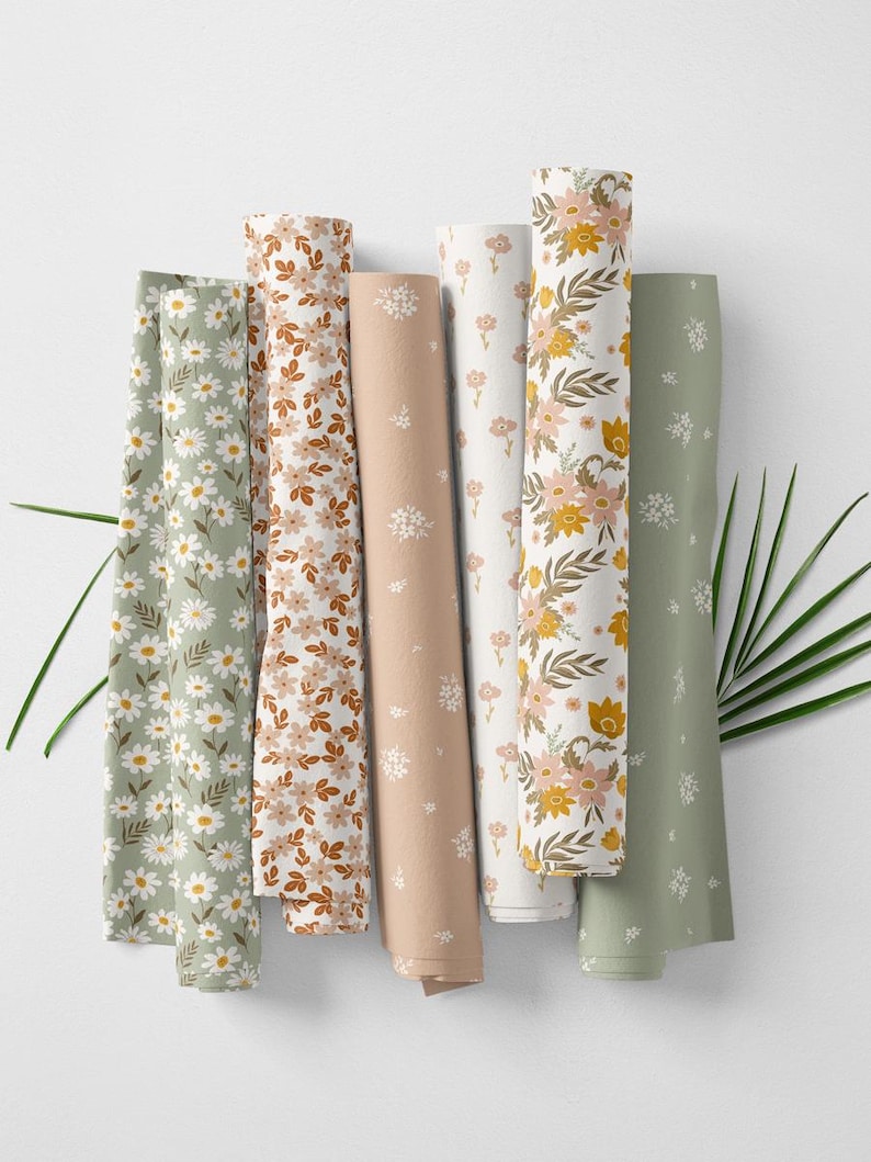 May include: Rolled fabric bolts in various floral patterns. Designs include daisies, small flowers, and larger blooms in shades of green, brown, peach, and white. The fabrics are arranged vertically against a white background.