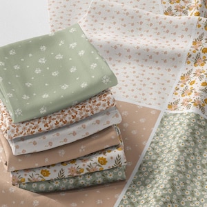 Puede incluir: Una pila de cuadrados de tela doblados con varios estampados florales y colores. Las telas incluyen tonos de verde, beige y blanco, con pequeños diseños de flores y hojas. Las telas están dispuestas sobre una pieza de patchwork más grande.