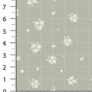 May include: A fabric sample with a grid pattern and white floral clusters. The background is a muted green color. The image includes a ruler with inch measurements along the left side and bottom.